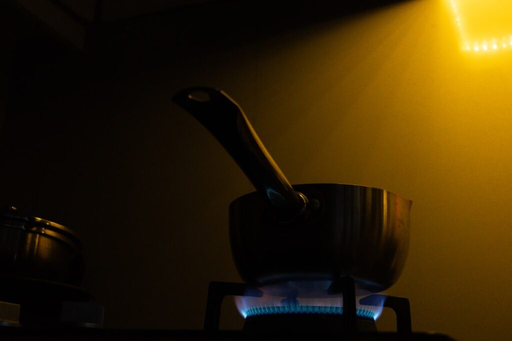 A person covering a small burning pan on a kitchen stove with a metal lid while wearing an oven mitt.