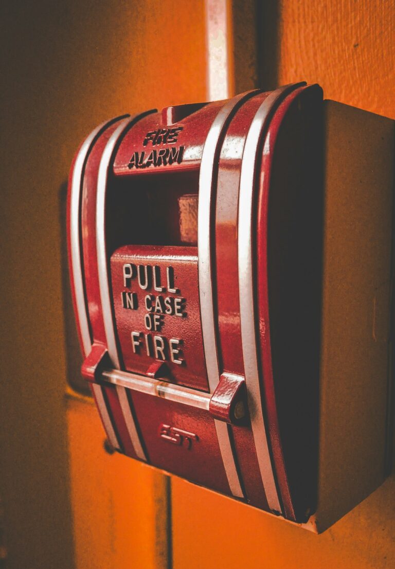 A person pressing the test button on a ceiling-mounted smoke detector in a residential hallway.