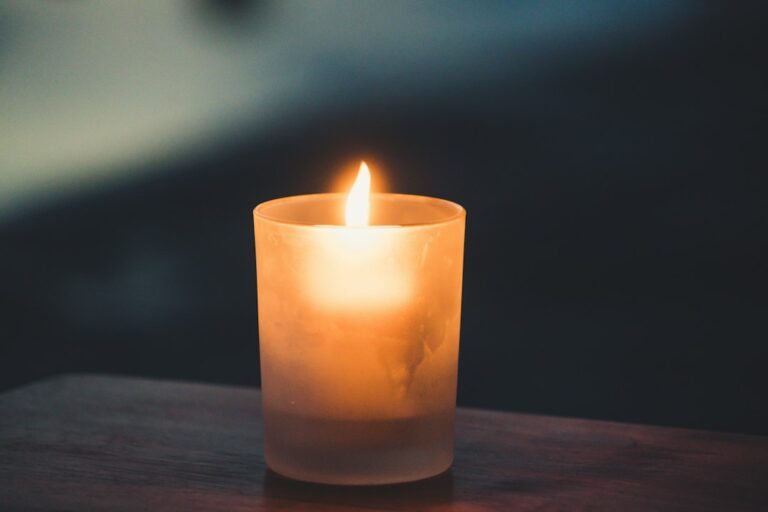 Adult extinguishing a candle on a stable table away from curtains, decorations, and other household items.